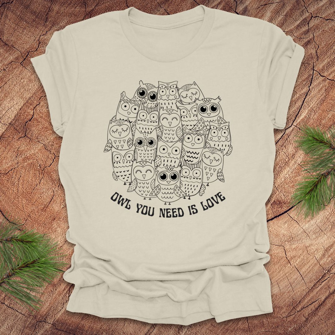Beige t-shirt with owl design and text 'OWL YOU NEED IS LOVE' on a wooden surface.