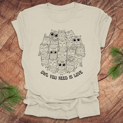 Beige t-shirt with owl design and text 'OWL YOU NEED IS LOVE' on a wooden surface.