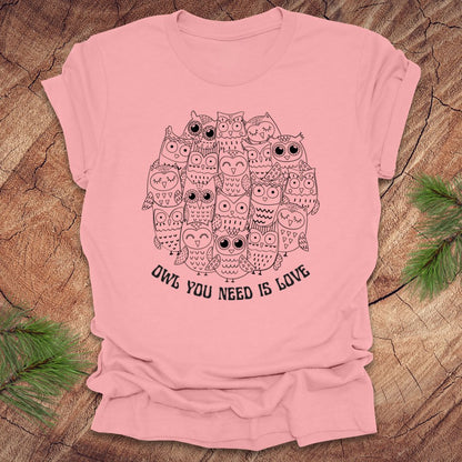 Pink t-shirt with owl design and text 'OWL YOU NEED IS LOVE' on a wooden surface.