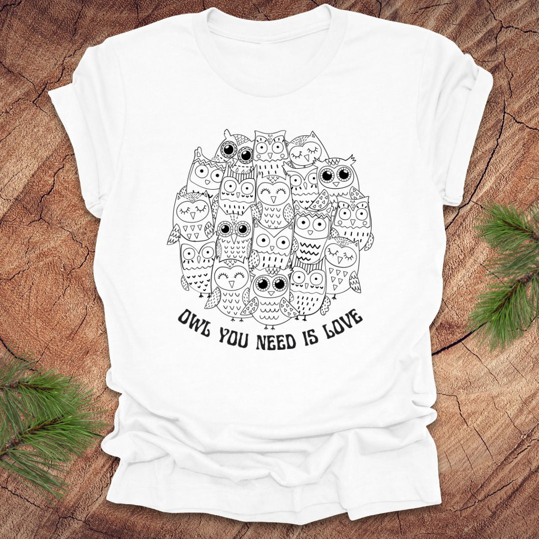 White t-shirt with owl design and text 'OWL YOU NEED IS LOVE' on a wooden surface.