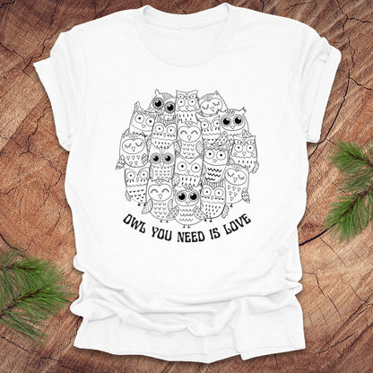 White t-shirt with owl design and text 'OWL YOU NEED IS LOVE' on a wooden surface.