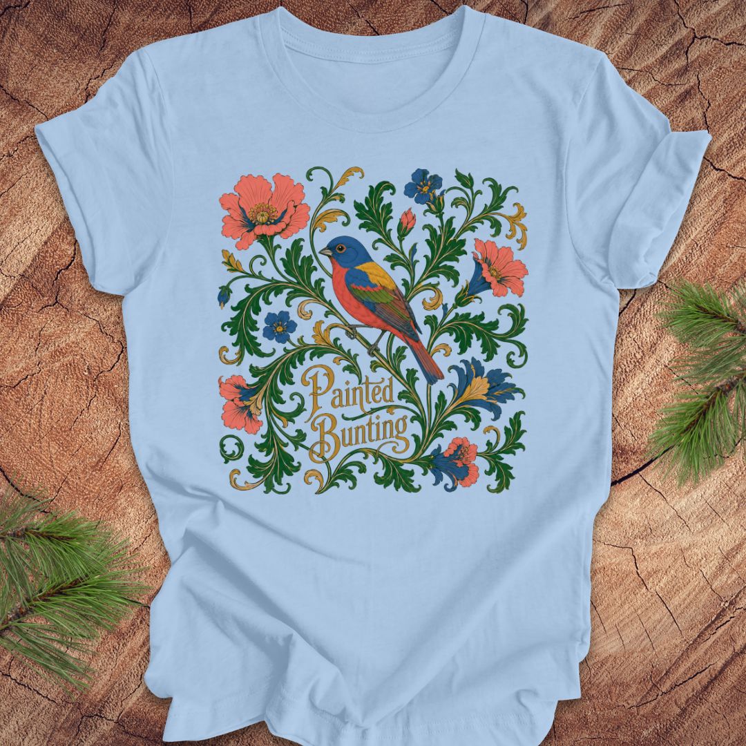 Blue t-shirt with a painted bunting bird and floral design on a wood background.