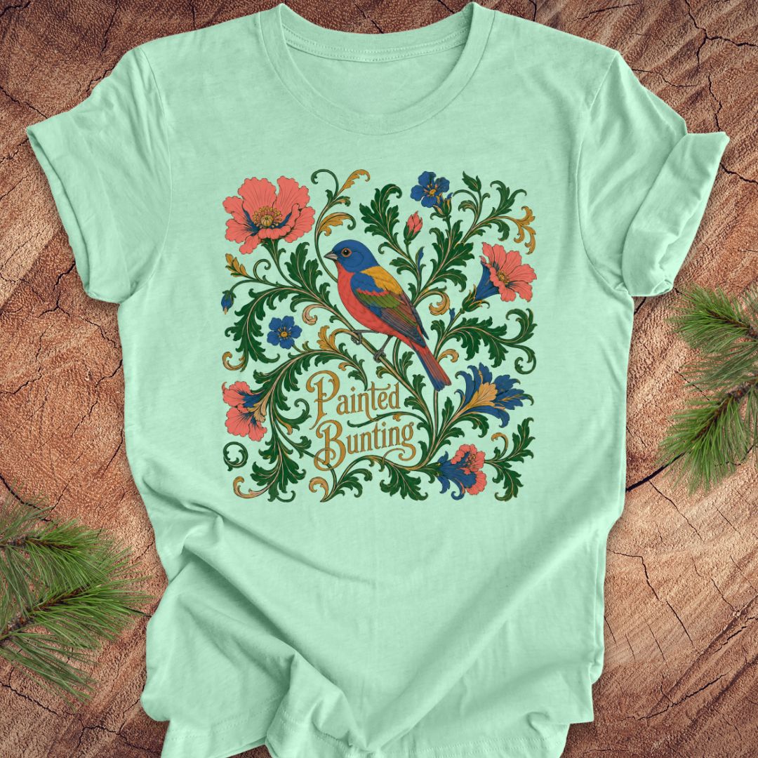 Mint green t-shirt with a painted bunting bird and floral design on a wood background.
