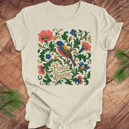 Beige t-shirt with a painted bunting bird and floral design on a wood background.