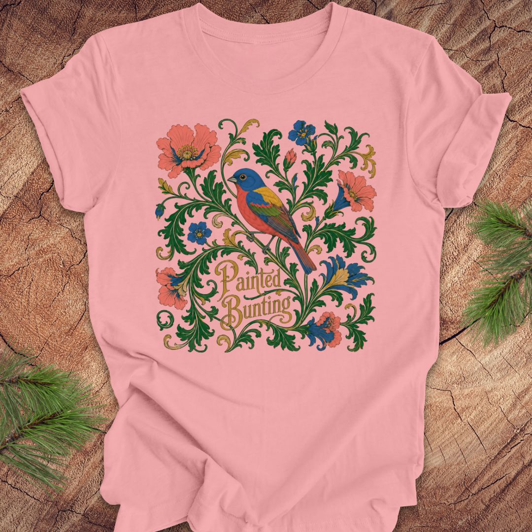 Pink t-shirt with a painted bunting bird and floral design on a wood background.