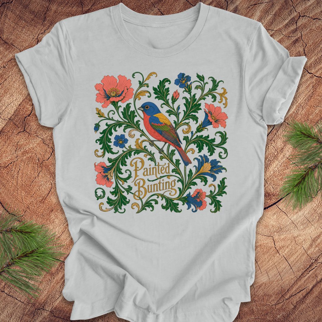Gray t-shirt with a painted bunting bird and floral design on a wood background.