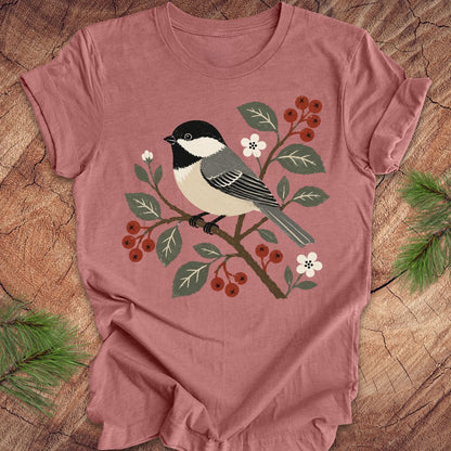Mauve t-shirt with a chickadee design on a wooden surface