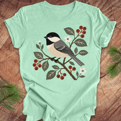 Mint green t-shirt with a chickadee and berry design on a wooden surface
