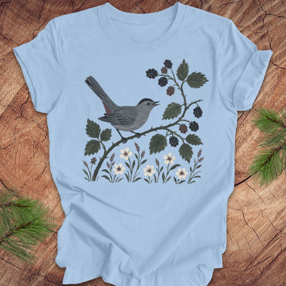 Light blue t-shirt with a catbird and branch design on a wooden surface