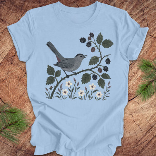 Light blue t-shirt with a catbird and branch design on a wooden surface