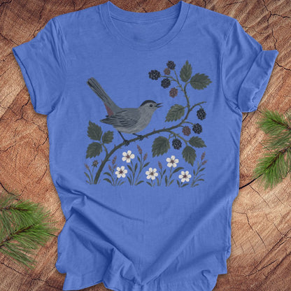 Blue t-shirt with a catbird and branch design on a wooden surface