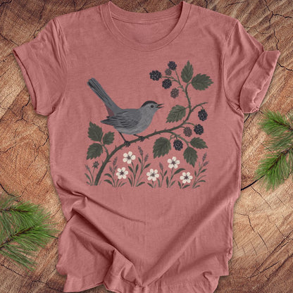 Mauve t-shirt with a catbird and floral design on a wooden surface