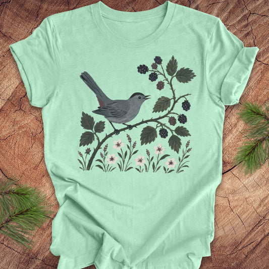 Mint green t-shirt with a catbird and branch design on a wooden surface