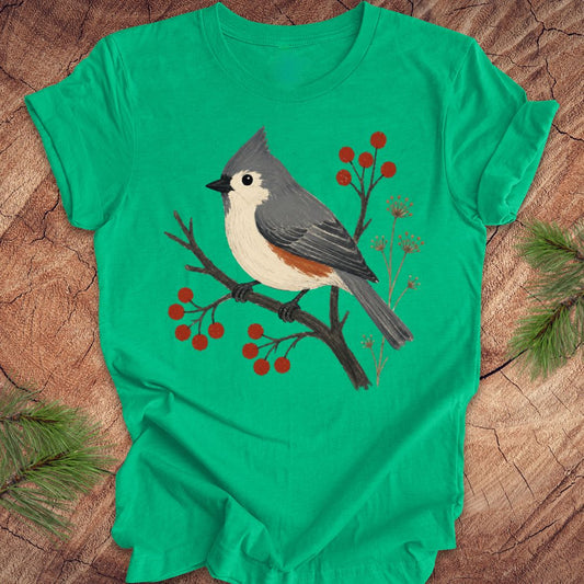 Green t-shirt with a titmouse and berries design on a wood background.