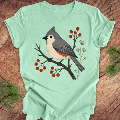 Mint green t-shirt with a titmouse and berries design on a wood background.