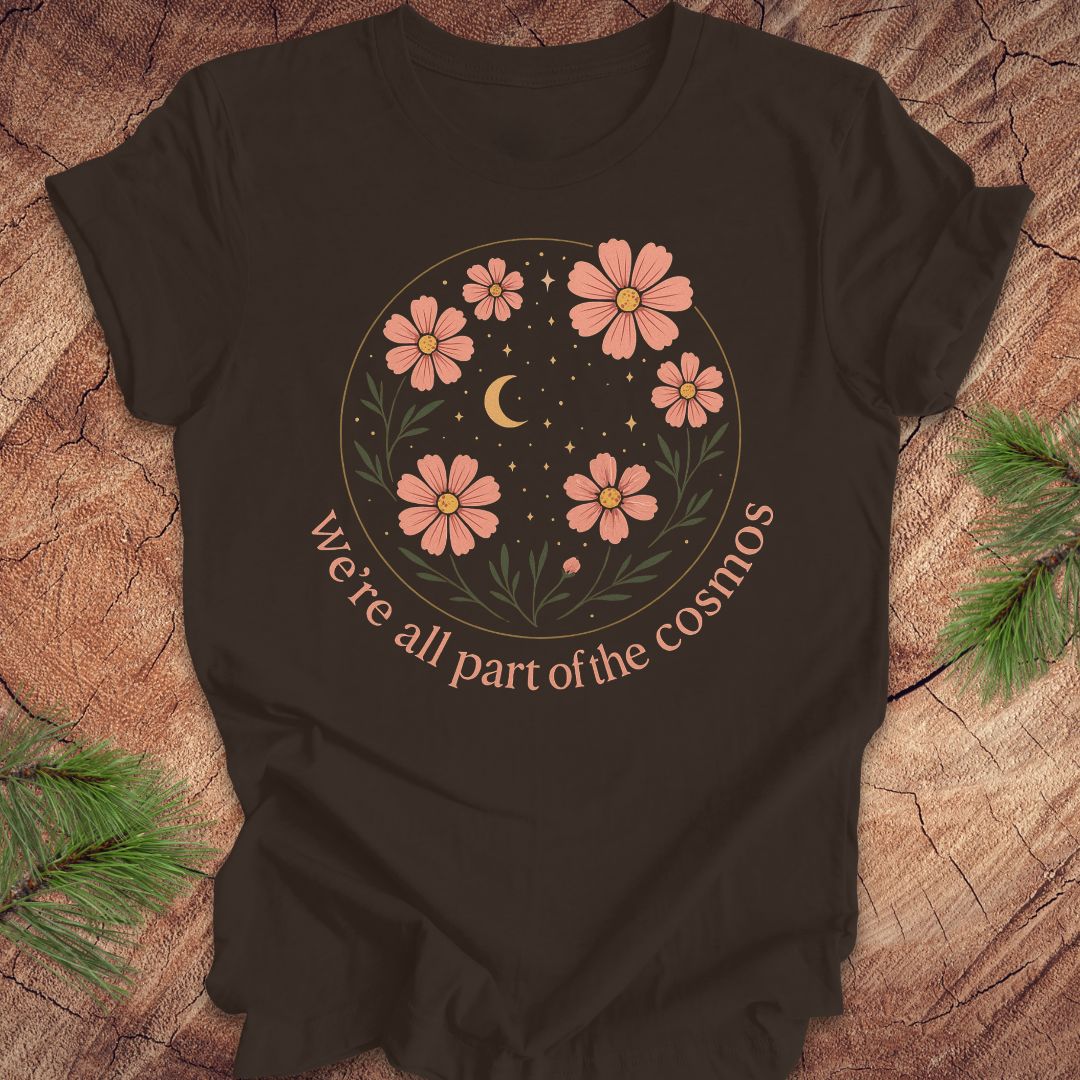 Brown t-shirt with moon and stars and text "we're all part of the cosmos" on a wood background.