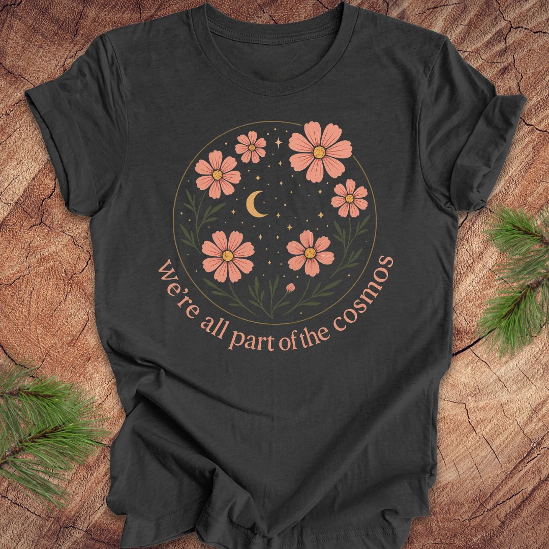 Gray t-shirt with moon and stars and text "we're all part of the cosmos" on a wood background.