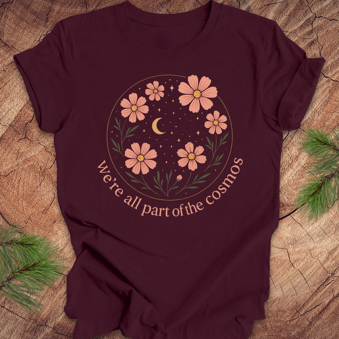 Maroon t-shirt with moon and stars and text "we're all part of the cosmos" on a wood background.