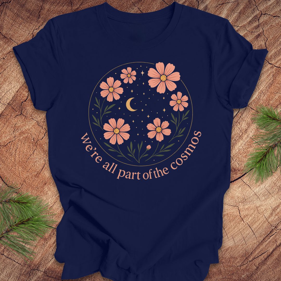 Navy blue t-shirt with moon and stars and text "we're all part of the cosmos" on a wood background.