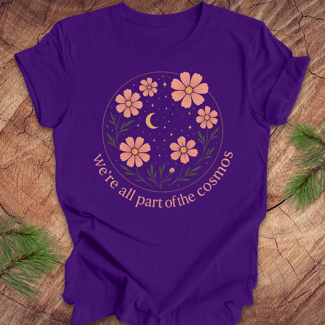 Purple t-shirt with moon and stars and text "we're all part of the cosmos" on a wood background.