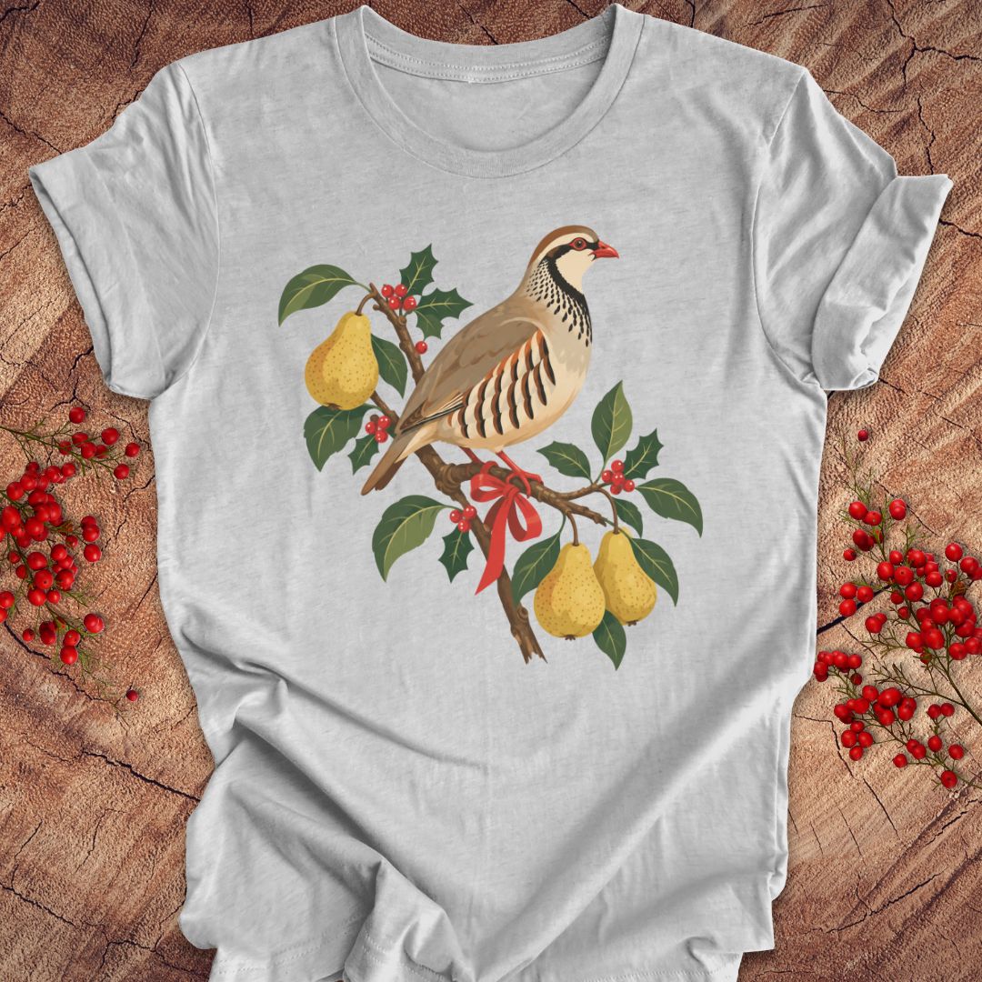 Athletic heather gray t-shirt with a partridge perched on a branch with golden pears, holly, red berries, and a red ribbon, laid flat on a rustic wood background with red winter berries.