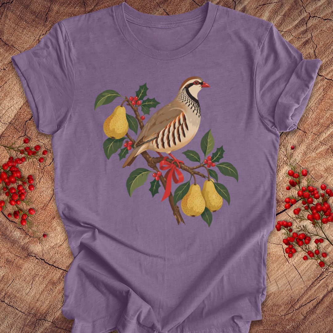 Heather purple t-shirt with a partridge perched on a branch with golden pears, holly, red berries, and a red ribbon, laid flat on a rustic wood background with red winter berries.