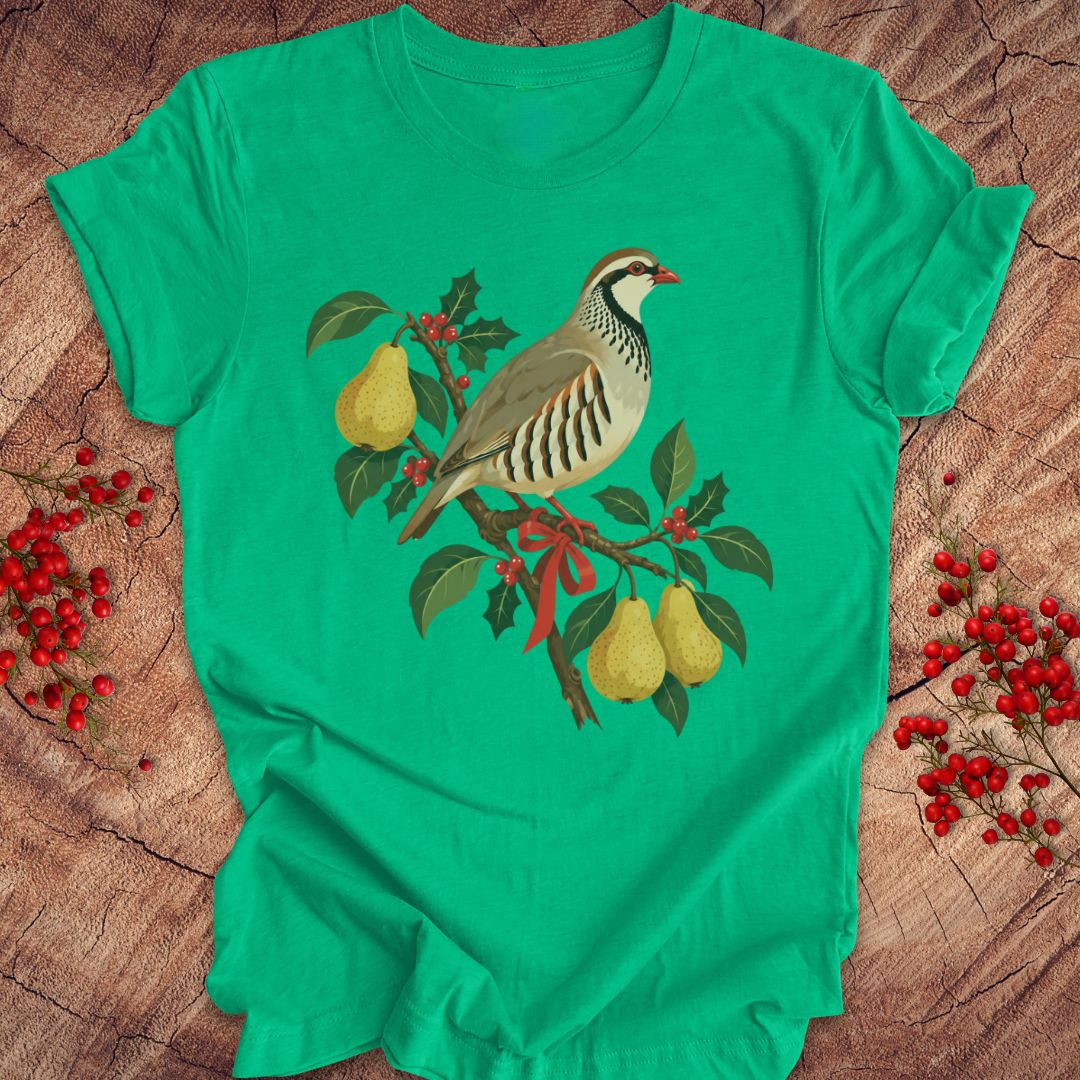 Heather kelly green t-shirt with a partridge perched on a branch with golden pears, holly, red berries, and a red ribbon, laid flat on a rustic wood background with red winter berries.