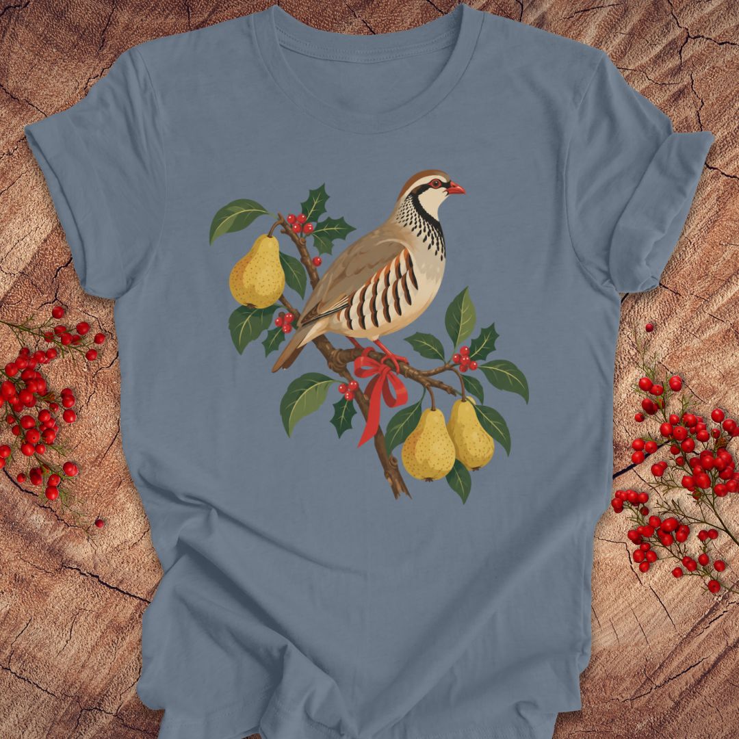 Steel blue t-shirt with a partridge perched on a branch with golden pears, holly, red berries, and a red ribbon, laid flat on a rustic wood background with red winter berries.