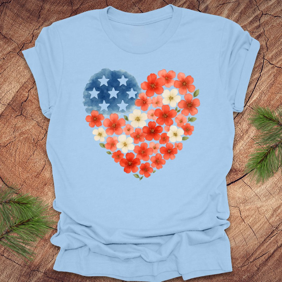 Baby blue t-shirt with a heart-shaped design featuring red, white and blue flowers and stars on a wooden surface.