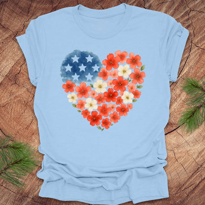 Baby blue t-shirt with a heart-shaped design featuring red, white and blue flowers and stars on a wooden surface.
