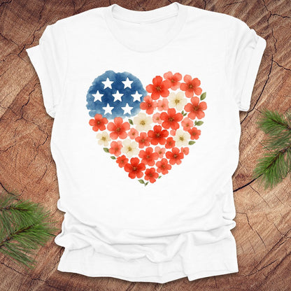 White t-shirt with a heart-shaped design featuring red, white and blue flowers and stars on a wooden surface.