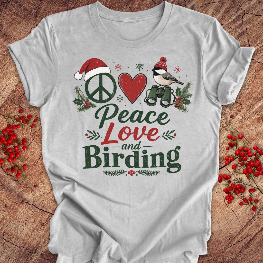 A light gray short-sleeve t-shirt with a festive Christmas-themed graphic that reads 'Peace Love and Birding'. The graphic features a peace sign with a Santa hat, a red heart, a bird with binoculars, and holiday greenery.