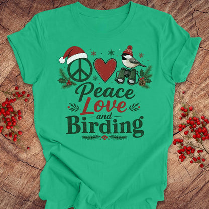 A bright green short-sleeve t-shirt with a festive Christmas-themed graphic reading 'Peace Love and Birding'. The graphic features a peace sign with a Santa hat, a red heart, a bird with binoculars, and holiday accents, displayed on a rustic wood background with red berries.
