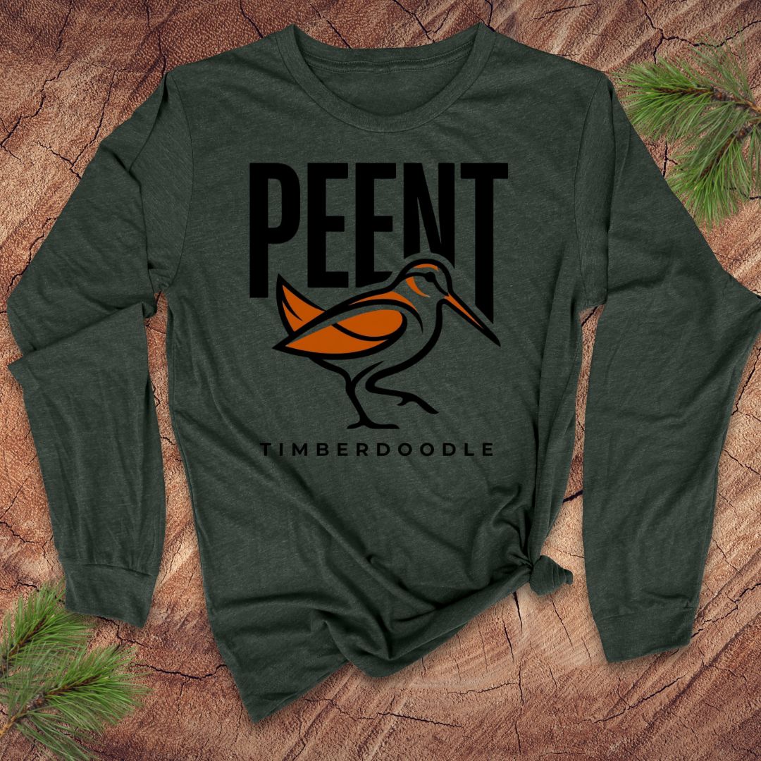 Green long-sleeve shirt with 'PEENT TIMBERDOODLE' logo on a wooden surface with pine branches.