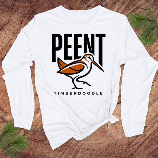 White long-sleeve shirt with 'PEENT' and 'TIMBERDOODLE' design on a wooden surface.