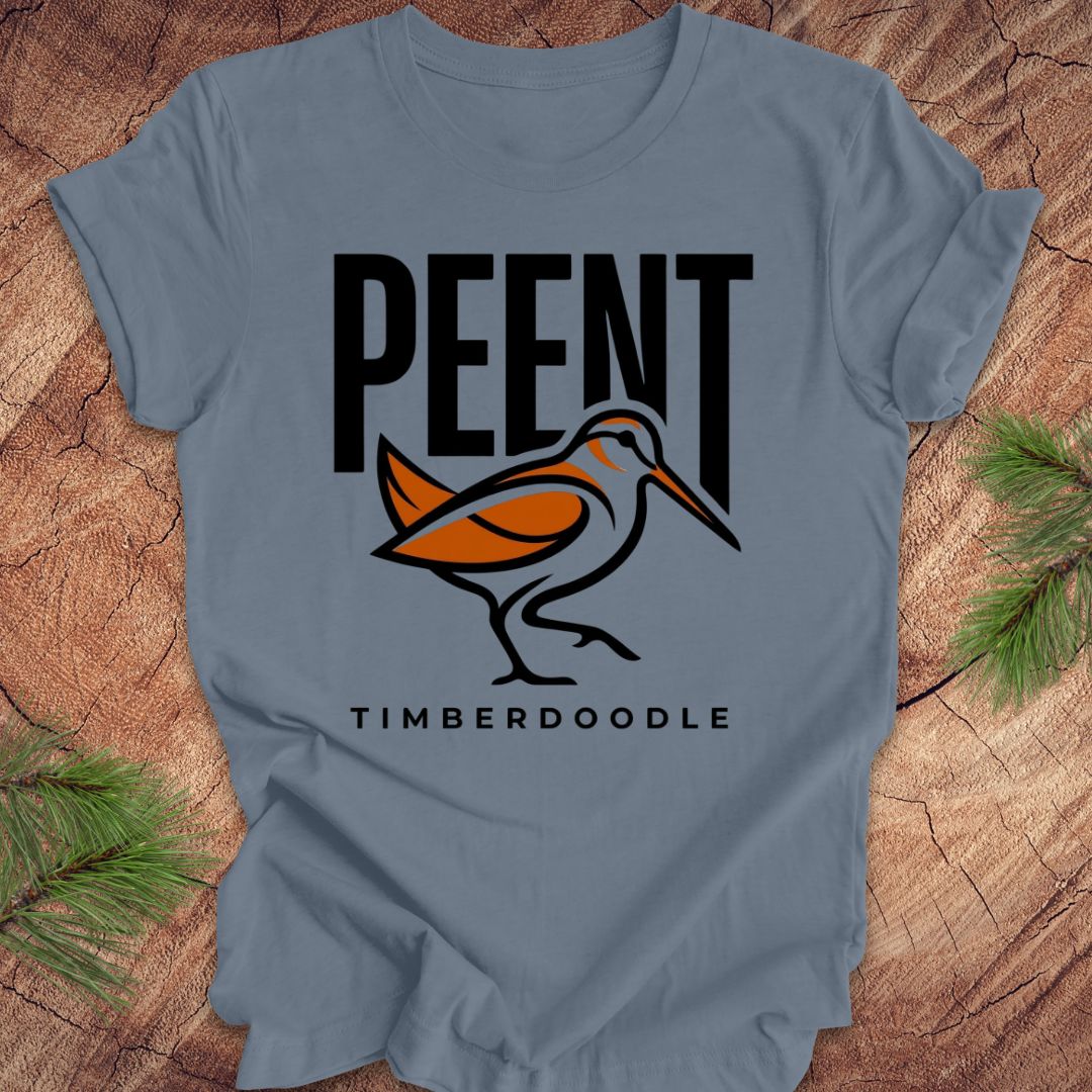 Steel blue t-shirt with 'PEENT' and 'TIMBERDOODLE' woodcock design on a wooden surface.
