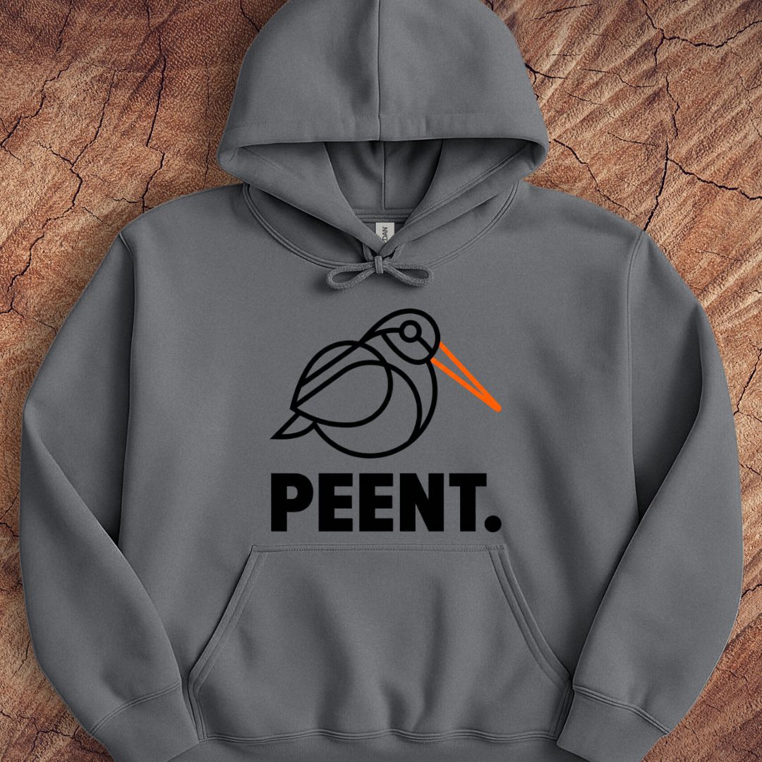 A dark gray pullover hoodie laid flat on a textured wood background. The hoodie features a minimalist black line art graphic of a bird with a bright orange beak, above the word 'PEENT.