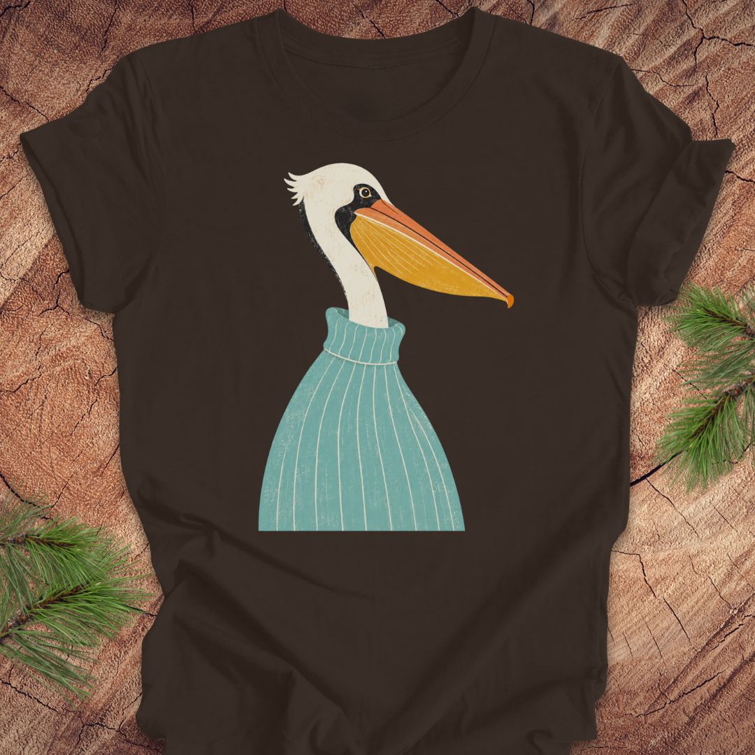 A dark brown short-sleeve t-shirt featuring a stylized graphic of a white pelican wearing a teal striped sweater, laid flat on a rustic wood background with pine branches in the corners.