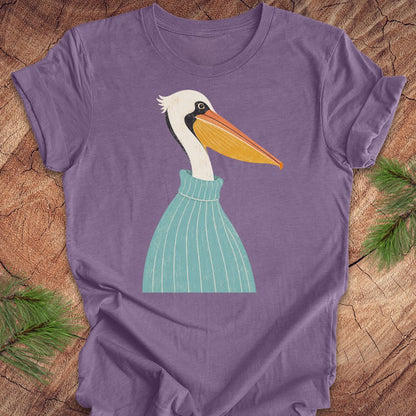 A purple short-sleeve crewneck t-shirt featuring a stylized graphic of a white pelican with a yellow-orange beak wearing a teal striped sweater, laid flat on a rustic wood background with pine branches in the corners.