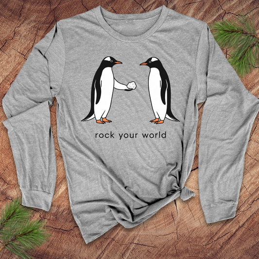 Gray long-sleeve t-shirt with penguins and text 'rock your world' on a wood background.