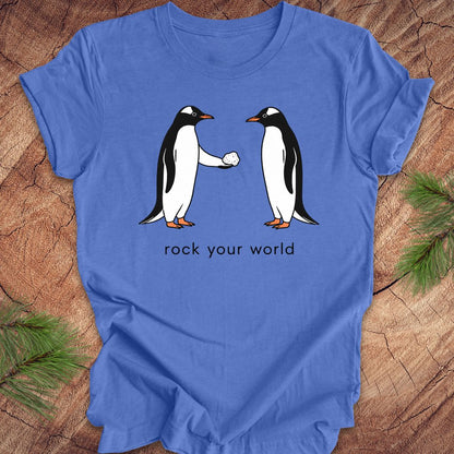 Blue t-shirt with a penguin handing another penguin a rock with text, 'rock your world' on a wood background.