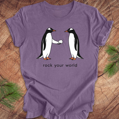 Purple t-shirt with a penguin handing another penguin a rock with text, 'rock your world' on a wood background.