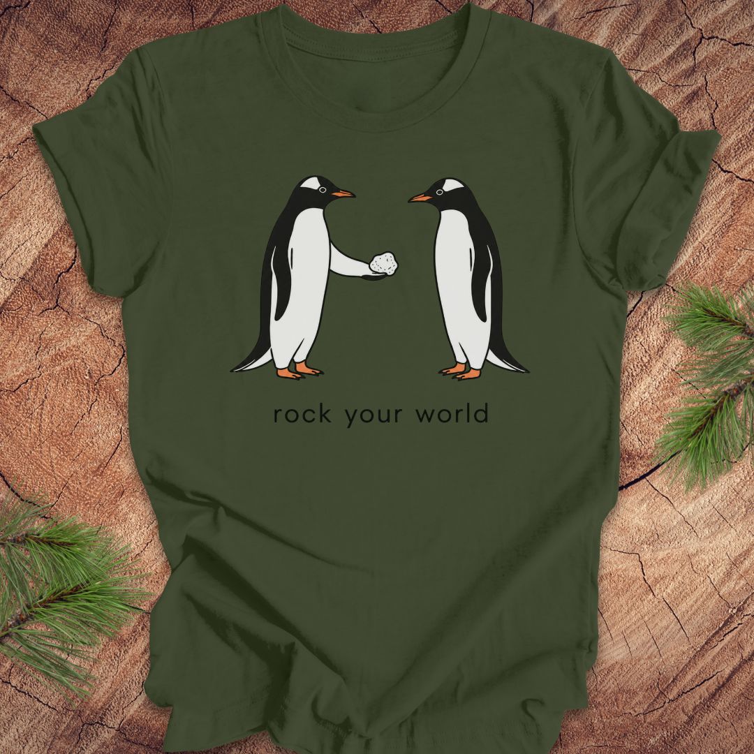 Green t-shirt with a penguin handing another penguin a rock with text, 'rock your world' on a wood background.