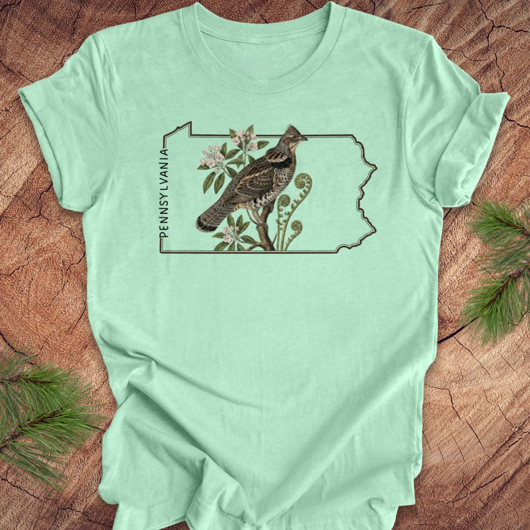 Mint green t-shirt with the state outline of Pennsylvania with ruffed grouse and floral design on a wooden surface