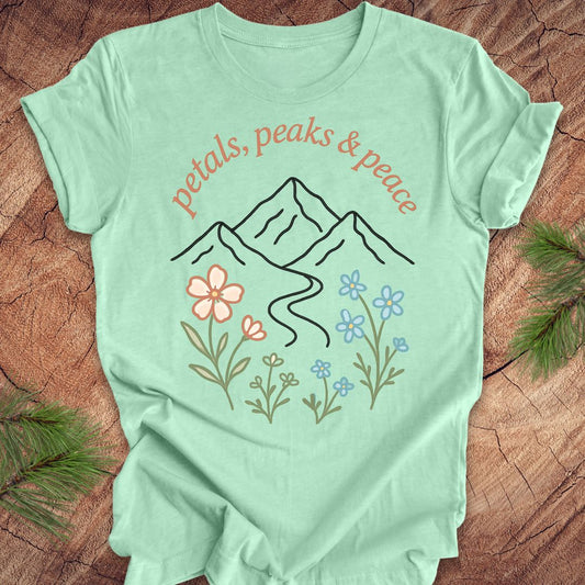 Mint green t-shirt with mountain and floral design on a wooden surface