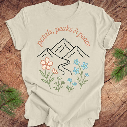 Beige t-shirt with mountain and floral design on a wooden surface