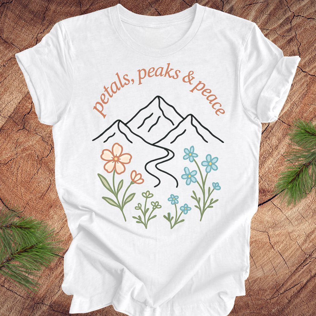 White t-shirt with mountain and floral design on a wooden surface