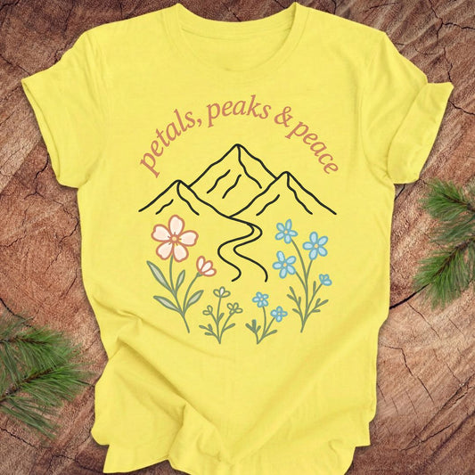 Yellow t-shirt with mountain and floral design on a wooden surface