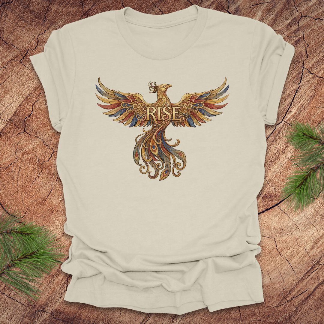 Beige t-shirt with a colorful phoenix design and 'RISE' text on a wooden surface.