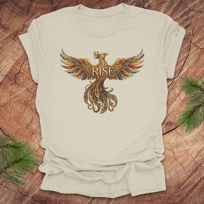 Beige t-shirt with a colorful phoenix design and 'RISE' text on a wooden surface.